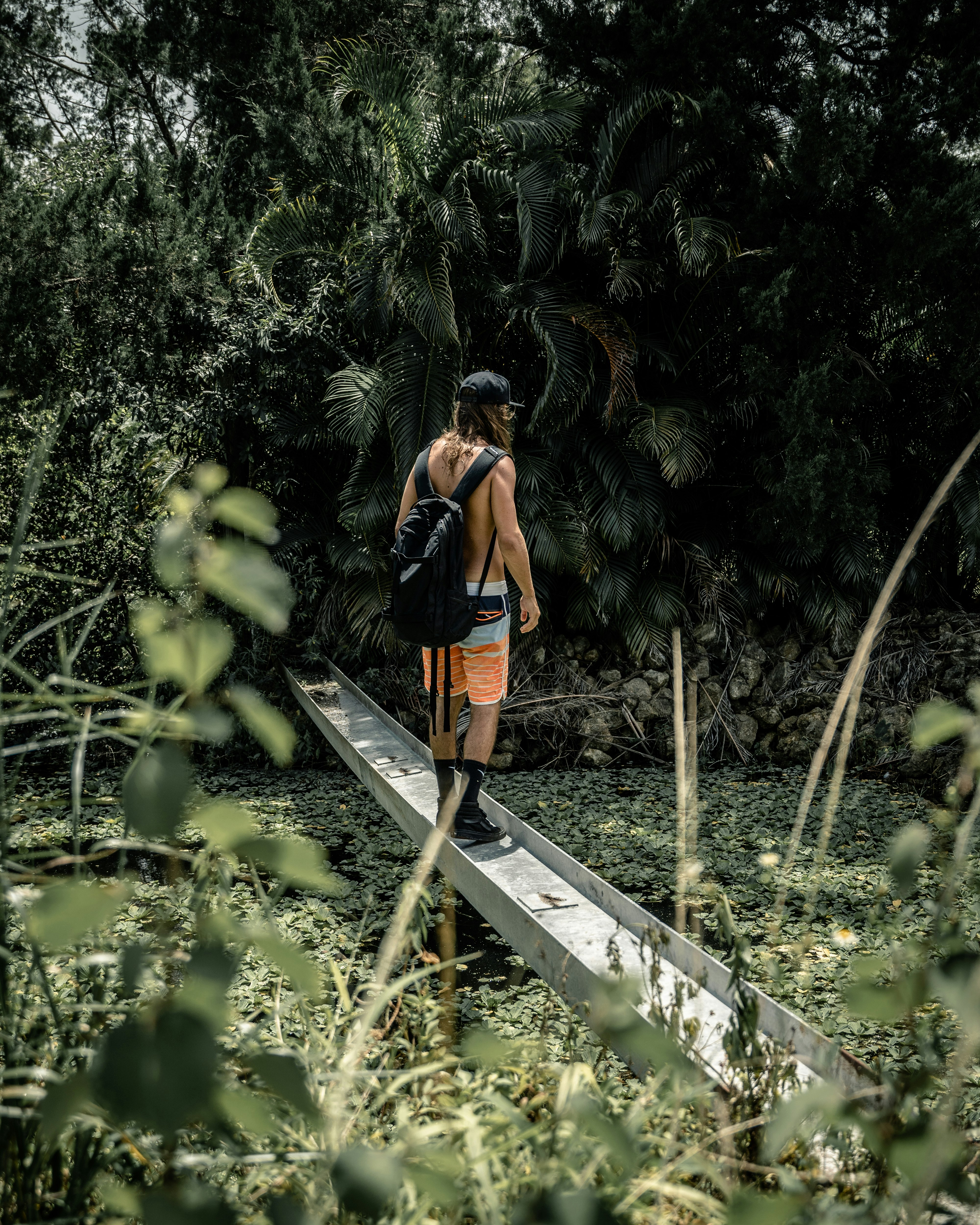 woman in orange and black backpack standing on brown wooden bridge surrounded by green plants during